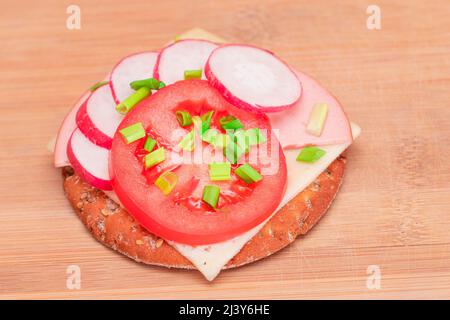 Panino Cracker croccante con pomodoro, salsiccia, formaggio, cipolle verdi e piatto sul tagliere. Colazione facile. Panini veloci e sani. Croccante con gustoso ripieno. Snack dietetico sano Foto Stock