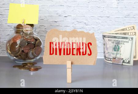 Mano che mette la moneta in vaso dividend parola con i soldi stack, concetto di finanza aziendale e investimenti. Foto Stock