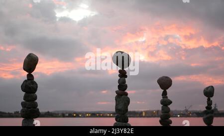 Bilanciamento della roccia contro cielo nuvoloso e drammatico al tramonto. Pila di pietre in equilibrio, piramide stabile nel crepuscolo rosa della sera. Nuvolosità al tramonto dall'acqua marina dell'oceano. Concetto di buddismo. Foto Stock