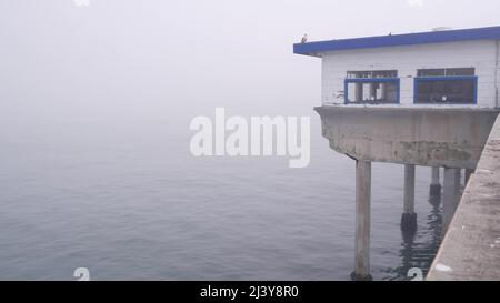 Casa di legno su pali, superficie d'acqua in foschia, Ocean Beach molo, nebbia costa della California, Stati Uniti d'America. Vecchio e obsoleto caffè sulla passerella abbandonata con il tempo mite. Tranquilla e silenziosa atmosfera sulla riva di San Diego. Foto Stock