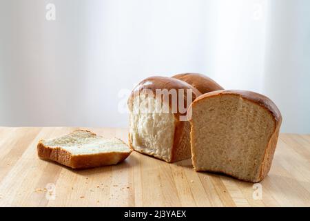 Una sola pagnotta di pane bianco fresco su un tagliere in legno in cucina. La calda e croccante panda ha fuso il burro sulla pagnotta croccante. Il bun è tagliato Foto Stock