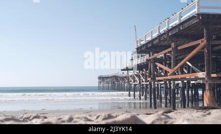 Sotto il molo in legno Crystal su pali, spiaggia oceano onde d'acqua, California USA. Vacanze estive sulla spiaggia di Mission, sulla riva di San Diego. Sotto il lungomare sulla costa del mare. Cinematografia senza giunture. Foto Stock