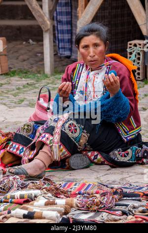 Donne peruviane, donna quechua che indossa abiti tradizionali delle Ande tessendo al mercato domenicale della città di Pisac, Valle Sacra, Perù. Foto Stock