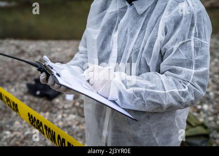 Primo piano sulle mani di sconosciuto uomo scena investigatore detective ispettore durante l'indagine raccolta di prove sulla scena del crimine forensics scrivere nel grafico Foto Stock