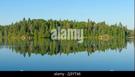 Riflessioni mattutine dei pini nel Bosco Nord sul Lago Saganagons nel Parco Provinciale Quetico in Ontario Foto Stock