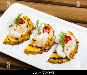 Fotografia di piatto con seppia fritto su una griglia con ananas, pomodori ciliegini e salsa Cile Foto Stock