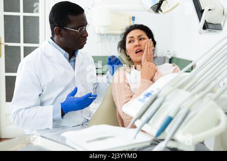 Paziente donna che è venuto ad un appuntamento con un dentista maschio è seduto in una sedia dentale in clinica ufficio, mostrando quale lato del suo dente dolori Foto Stock