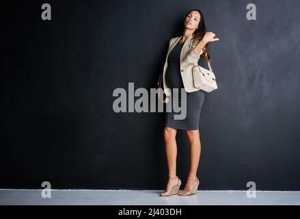 Im riuscito per due di noi ora. Studio ritratto di una giovane donna d'affari incinta in piedi su uno sfondo nero. Foto Stock