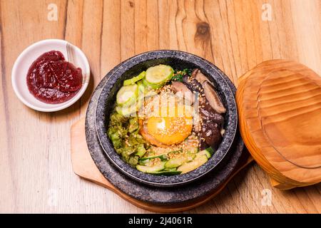 Bibimbap in una ciotola di pietra riscaldata nera, piatto tradizionale coreano - Bibimbap riso misto con verdure includono manzo e uova fritte, cibo giapponese caldo pentola Foto Stock