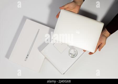 Saratov, Russia - 26 febbraio 2022: Tenere in mano MacBook Air da 13 pollici con processore M1, confezione con accessori di ricarica, sfondo bianco Foto Stock