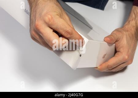 Saratov, Russia - 26 febbraio 2022: Staccare l'involucro dalla confezione del nuovo MacBook Air da 13 pollici con primo piano del processore M1, sfondo bianco Foto Stock