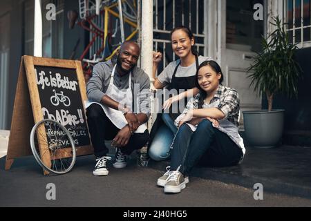 Abbiamo ottenuto quello che volete. Ritratto di tre giovani lavoratori seduti al di fuori del negozio di riparazione biciclette. Foto Stock