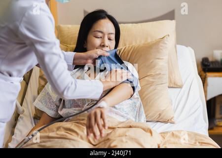 Infermiere che assume la pressione sanguigna di una paziente matura nel letto d'ospedale. Foto Stock