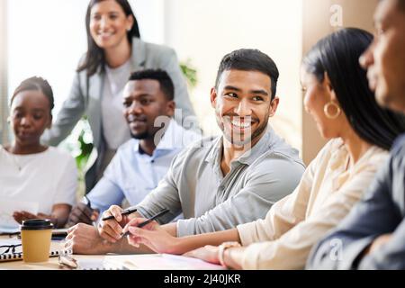 È andata bene, non dici. Scatto corto di un bel giovane uomo d'affari seduto con i suoi colleghi nella sala riunioni durante una riunione. Foto Stock