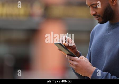 Uomo con pelle nera scritta sullo schermo dello smartphone con penna digitale in strada Foto Stock