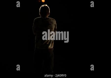 Silhouette di un uomo al buio. L'uomo sul palco. Retroilluminazione. Oscurità sul palco. L'uomo si alza con la schiena. Foto Stock