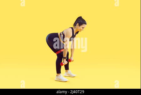 Donna che fa esercizi sportivi con manubri e con elastico fitness band su sfondo giallo. Foto Stock