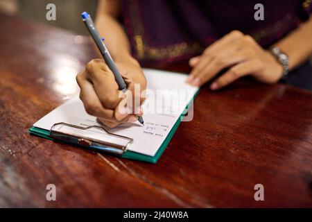 È ora di effettuare il check-in. Primo piano di una donna che compila un modulo per il check-in in hotel su una clipboard presso il banco della reception dell'hotel. Foto Stock