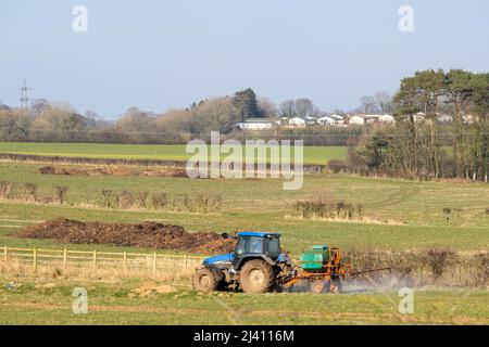 Irvine, Scotland, UK - 25 marzo 2022: Gli Farmlands scozzesi con un trattore New Holland che irrorano i campi con Cunninghamhead Retirement Village e pi Foto Stock