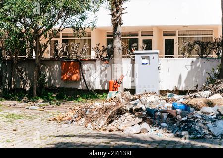 Mucchio di macerie di rifiuti di fronte all'edificio residenziale. Scatola fusibili circondata da rifiuti. Rifiuti domestici detriti sparsi fuori dal residenziale Foto Stock