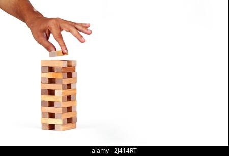 La mano dell'uomo ha messo un blocco alla pila della torre dai blocchi di legno del giocattolo con sfondo isolato. Foto Stock