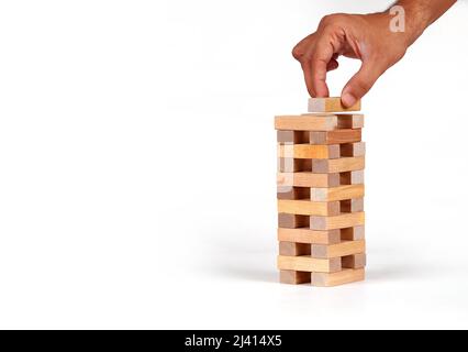 La mano dell'uomo ha messo un blocco alla pila della torre dai blocchi di legno del giocattolo con sfondo isolato. Foto Stock