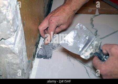 Un operaio mette una spatola sul pavimento quando posano le mattonelle di pavimento di ceramica. Messa a fuoco selettiva Foto Stock