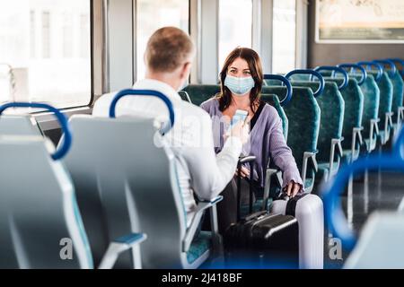 Un paio di amici che indossano la maschera e parlano bene mentre si viaggia in treno Foto Stock