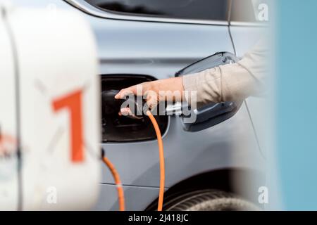 Una giovane donna che carica un'auto elettrica in ambienti urbani Foto Stock