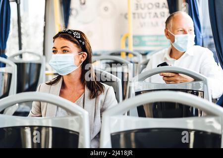 Viaggiatori che indossano maschere protettive che viaggiano con autobus pubblico Foto Stock