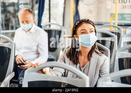 Viaggiatori che indossano maschere protettive che viaggiano con autobus pubblico Foto Stock