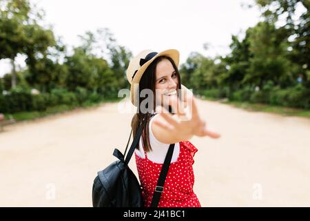 Felice giovane donna che si allunga la mano alla macchina fotografica e sorride nel parco pubblico Foto Stock