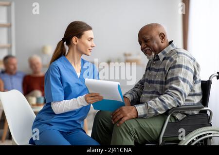 Donna graziosa nel workwear che aiuta l'uomo anziano nero che riempie le carte Foto Stock