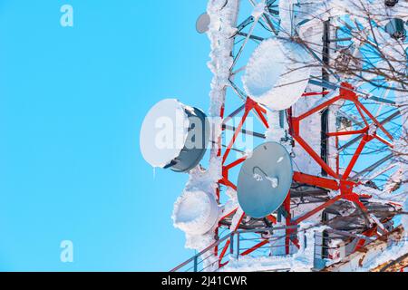 Antenne della torre di comunicazione ricoperte di neve con cielo blu come spazio di copia Foto Stock