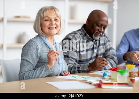 Donna anziana positiva che ama dipingere con pennello Foto Stock