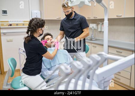 Dentista curante il paziente maschile in clinica dentale Foto Stock