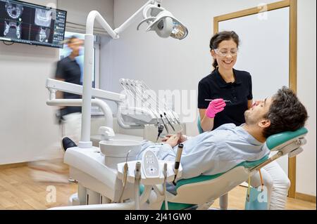Dentista curante il paziente maschile in clinica dentale Foto Stock