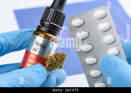 Scienziato tenere e confrontare CBD olio di cannabis e fiore germoglio in una mano e pillole mediche blister in altri Foto Stock