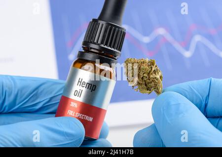 Lo scienziato tiene la canapa pieno olio di spettro in una mano e CBD cannabis fiore in altra Foto Stock