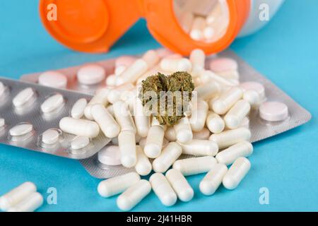 CBD germoglio di fiori di cannabis su cumulo di capsule da flacone aperto e blister pillole mediche su sfondo blu Foto Stock