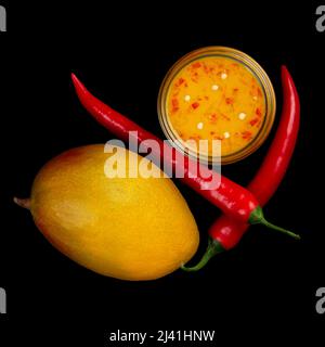 Salsa al peperoncino mango, mango maturo e due peperoni rossi caldi isolati sul nero Foto Stock