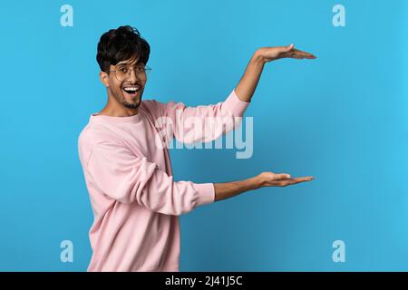 Un ragazzo indù positivo che tiene qualcosa di invisibile nelle sue mani Foto Stock
