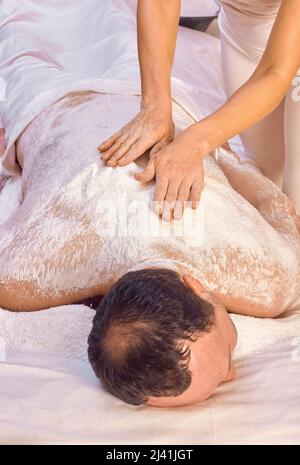 Una donna guaritrice esegue un rituale con sale, sfrega la schiena di un uomo bugiolo con sale. Relax. Foto Stock