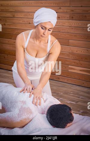 Una donna guaritrice esegue un rituale con sale, sfrega la schiena di un uomo bugiolo con sale. Relax. Foto Stock