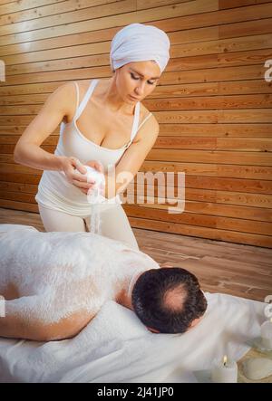 Una donna guaritrice esegue un rituale con sale, versa il sale sulla schiena di un uomo menzogna. Relax. Foto Stock