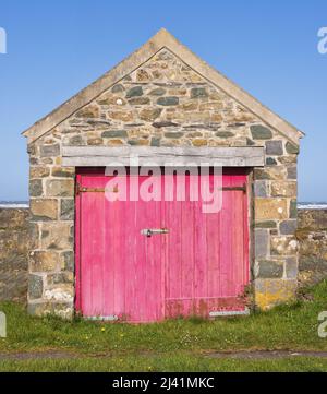 Garage in pietra gallese con porte in legno rosa usurate. Foto Stock