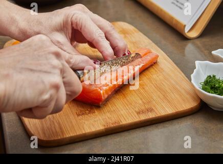 Lo chef taglia il salmone con il coltello per preparare la ricetta Foto Stock