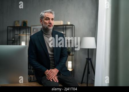 Uomo d'affari mature e triste seduto sulla scrivania e pensando al chiuso in ufficio. Foto Stock
