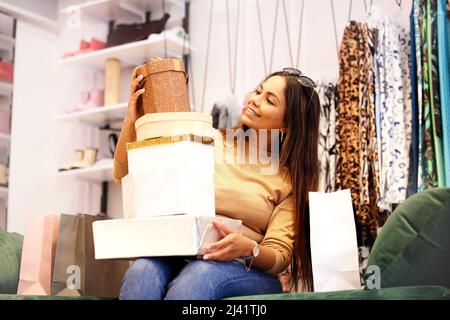 Sentendosi blu uscire e viziarsi. Scatto di una giovane donna seduta in un negozio con scatole regalo impilate sul suo grembo. Foto Stock