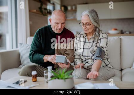 Coppia anziana a casa che misura la pressione sanguigna. Foto Stock